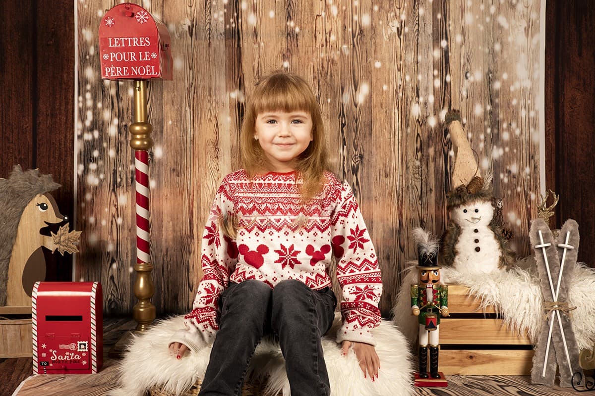 Exemple de portrait : un enfant assis dans le décor de Noël, fond en bois, boîte aux lettres du Père Noël et bonhomme de neige